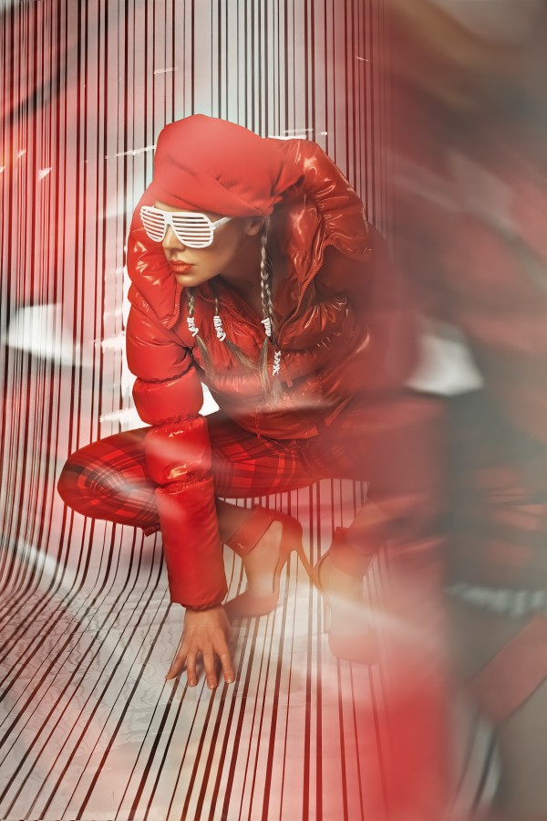 Beautiful blonde fashion model wearing braids in a red outfit with grill glasses posing in a white striped plastic environment by Artmood Visualz